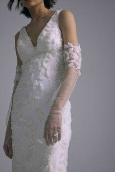 a woman in a white wedding dress with gloves on her arm and one hand holding something