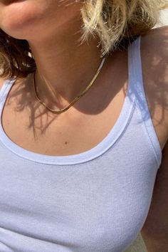 a close up of a person wearing a white tank top with a gold necklace on her neck