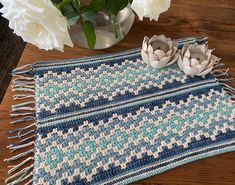 a crocheted blue and white placemat next to flowers on a wooden table