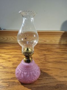 a pink glass vase sitting on top of a wooden table next to a lamp shade