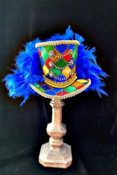 Add a bit of Parumpumpum to your Christmas decor with this stunning Nutcracker Mini Top Hat! This little gem is the perfect topper for your holiday mannequin or shop display! The rhinestone buttons and gold chains add the touch of glam and the royal blue feathers finish the look. This beauty measures approximately 4.5 inches tall x 7 inches wide x 7 inches deep. Decorative Hats, Brighton Pride, Art Hats, Costume Closet, Tea Hats, Mini Hats, Parrot Head, Headpiece Diy, Blue Feathers