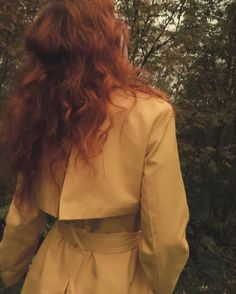 the back of a woman's head with long red hair in a trench coat