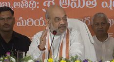 the man is giving a speech in front of other men at a table with flowers on it