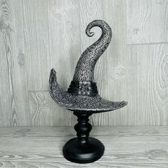 a black and white photo of a witches hat on a stand in front of a wooden wall