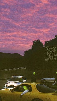 a yellow car parked in front of a parking lot at dusk with the sky painted pink and purple