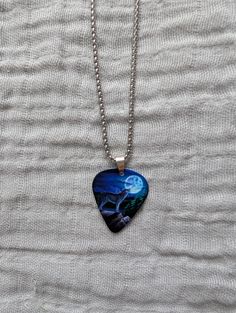 a heart shaped necklace with a blue and black painting on the front, sitting on top of a white sheet