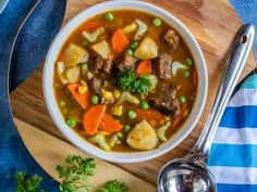 a bowl of beef stew with carrots, potatoes and parsley on a wooden cutting board