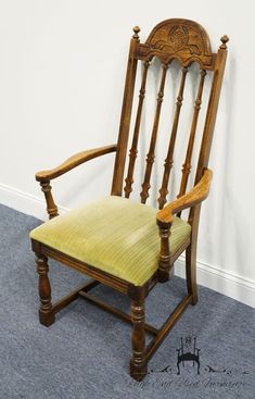 an old wooden chair with a green seat pad on the floor next to a white wall