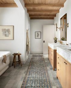 a long hallway with wood ceilinging and white walls, leading to a large bathroom