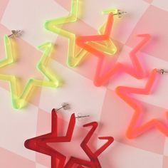 three neon star shaped earrings sitting on top of a pink checkered tablecloth covered floor