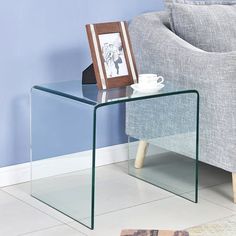 a glass side table with a coffee cup on it in front of a gray couch