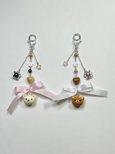 three key chains with charms attached to them on a white surface, one has a teddy bear and the other has a bow