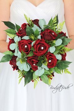 a bride holding a bouquet of red roses and greenery on her wedding day,