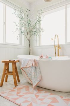 a white bath tub sitting next to a wooden stool in a bathroom under a window