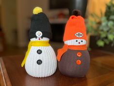 two knitted snowmen sitting on top of a wooden table next to each other