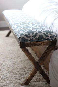 a bed with a bench sitting on top of it next to a white rug and pillows