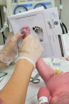 a person with gloves on holding up a piece of paper next to a baby's foot