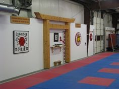 an indoor gym area with blue and red mats on the floor, white walls, and wood framed doorways