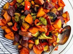 a glass bowl filled with cooked vegetables on top of a white table cloth next to a spoon