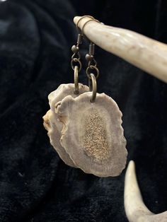 a piece of wood hanging from a metal hook on a black cloth with two horns in the background