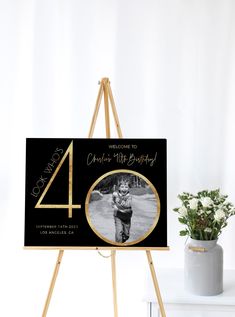 a wooden easel with a black and gold birthday card on it next to a potted plant