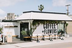 a coffee and flowers sign on the side of a building next to a sidewalk with benches