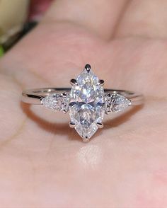 a woman's hand holding a ring with a pear shaped diamond in the center