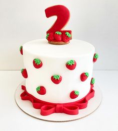 a two tiered cake with strawberries on it and a number one topper