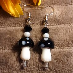 a pair of black and white mushroom earrings on a brown blanket next to a yellow flower