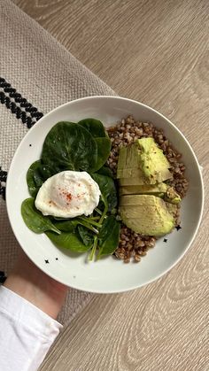 a white plate topped with spinach and an avocado on top of brown rice