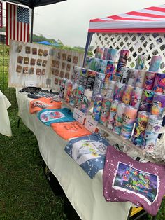 the table is set up with many items for sale at this outdoor event, including t - shirts and mugs