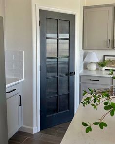 a kitchen with gray cabinets and white counter tops next to a black glass front door