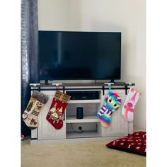 a flat screen tv sitting on top of a white entertainment center with stockings hanging from it's sides