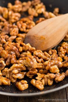 walnuts are being cooked in a skillet with a wooden spoon on the side