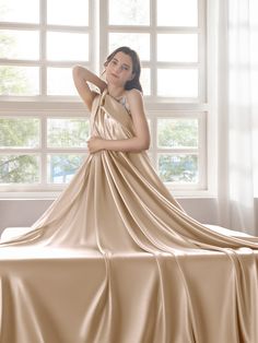 a woman in a tan dress is sitting on a bed with her arms behind her head