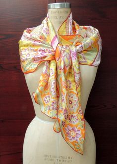 "Vintage \"Sunshine\" Scarf. Perfect for Festival Fashions. This lovely retro headscarf is printed on medium weight fabric, Most likely polyester? It has some \"body\" to it probably because of the fabric content and it is printed with an overlay of gold lurex outlining certain areas of the design. It is printed in a very usable pallet of oranges, yellows, greens and purple, on a off-white ground. It has a stylized floral design, with striped diagonal elements in the background and with a machine over-locked hem, that lettuces in areas of the curve- makes for wonderful styling configurations and makes a great cover up! Sash style, retro scarf is a generous (approx) 76 x 16 inches, at it's widest point, it is an interesting overall shape, with an undulating hem line- see photos.   This scar Vintage Silk Scarf For Summer Gift, Vintage Silk Scarf Summer Gift, Vintage Scarves For Summer Festivals, Vintage Summer Scarves For Festivals, Vintage Shawl Scarves For Summer, Vintage Summer Shawl Scarves, Yellow Bohemian Bandana For Summer, Vintage Summer Shawl Scarf, Vintage Yellow Silk Scarf