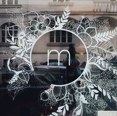 the reflection of a woman standing in front of a window with flowers and leaves on it