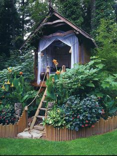 a garden shed with lots of plants and flowers in the foreground, surrounded by greenery