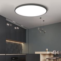 a modern kitchen with black cabinets and white counter tops is lit by an oval light fixture