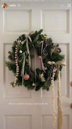 a wreath hanging on the front door with ribbons and ornaments around it's edges