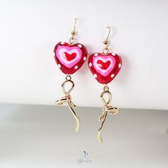 These unique lamp worked glass heart earrings feature cute red lamp work glass bead with 18k gold plate bowtie dangle drop charm and stainless steel ear wire. The elegant lamp work heart glass bead and bowtie earrings are the perfect gift for your loved on Valentine's occasion, a sweet heart for your sweetheart. Add these unique lollipop heart earrings to your everyday fashion earrings collection and match with your daily outfit to make a great statement. Dimensions: 2.77 x 0.78 inMaterial: Lamp worked glass, gold plated brass, stainless steel Jewelry Care: See more information about how to care for your jewelry here. Shipping Policy: Orders will be shipped within 1-3 business days. Economy shipping will take 7-14 days to arrive and standard shipping is 1- 4 days for U.S. orders. Internati Whimsical Jewelry For Valentine's Day Gift, Yellow Gold Heart Earrings For Valentine's Day Party, Cute Gold Heart Earrings For Gift, Heart Shaped Drop Earrings For Valentine's Day, Heart-shaped Drop Earrings For Valentine's Day, Drop Earrings Jewelry Gift For Valentine's Day, Whimsical Red Jewelry With Matching Earrings, Cute Jewelry For Valentine's Day Party, Elegant Jewelry With Red Bow For Gifting