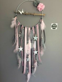 a pink and grey dream catcher hanging on a wall next to a stick with flowers