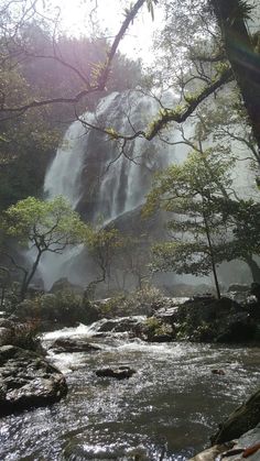 the sun shines through the trees and water as it flows over rocks in front of a waterfall