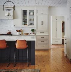 a kitchen with white cabinets and wooden floors, two bar stools at the island