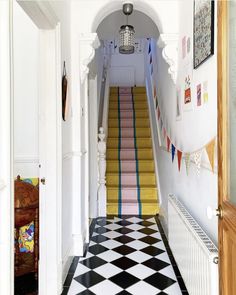 a hallway with black and white checkered flooring, yellow stairs and colorful rugs