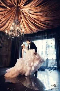 a bride and groom standing under a chandelier in front of a large window