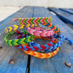 four bracelets are sitting on top of a wooden table and one is made out of multicolored fabric