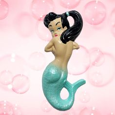 a little mermaid figurine sitting on top of a pink surface with bubbles in the background