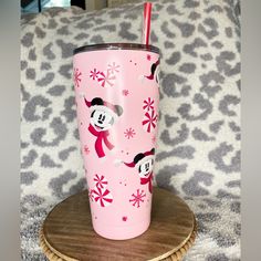 a pink tumbler with minnie mouse and snowflakes on it sitting on a wooden coaster