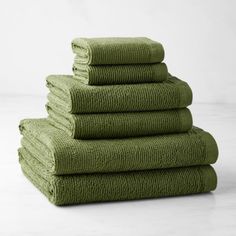 six folded towels stacked on top of each other in different shades of green, against a white background